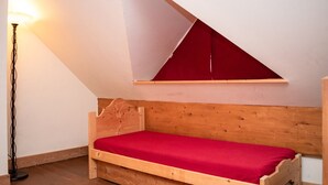 Una cama de madera pequeña en una habitación con techo inclinado y una ventana triangular roja.