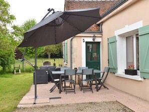 An outdoor patio with a table and chairs, a large umbrella, and a house with green shutters. - Charming renovated country house with WiFi and pets allowed (Saint-Calez-en-Saosnois)