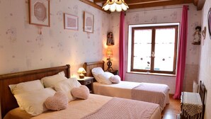 A room with two beds, a window with pink curtains, and a wooden ceiling.