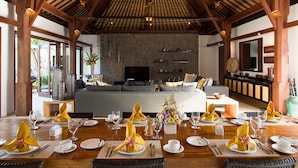 A spacious room with a large bed, a television, and a dining area set for a meal. - Villa Lilibel (Seminyak)