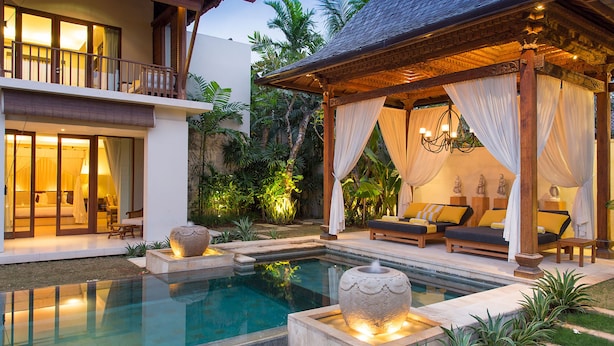 A pool with a stone fountain, a covered seating area with cushions, and a bedroom with a canopy bed. - Villa Lilibel (Seminyak)