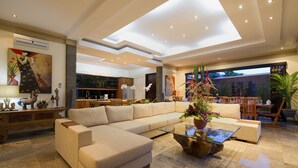Amplia sala de estar con un sofá modular grande, una mesa de centro de vidrio y una cocina moderna al fondo.