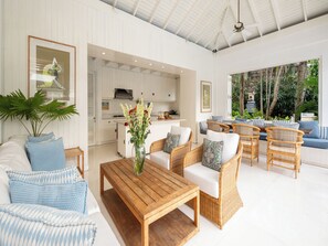 A spacious living area with a wooden coffee table, wicker sofas, and a large window overlooking a lush garden. - Villa Lulito (Seminyak)