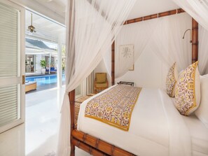 A bedroom with a canopy bed, a view of the pool, and a chair by the window. - Villa Lulito (Seminyak)