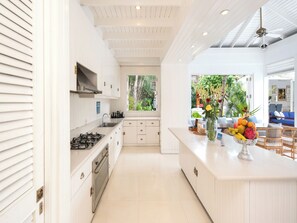 A modern kitchen with white cabinetry, a central island, and a view of the outdoors. - Villa Lulito (Seminyak)