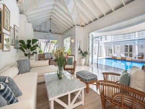 Amplia sala de estar con piscina, mobiliario blanco y vistas al área de la piscina.