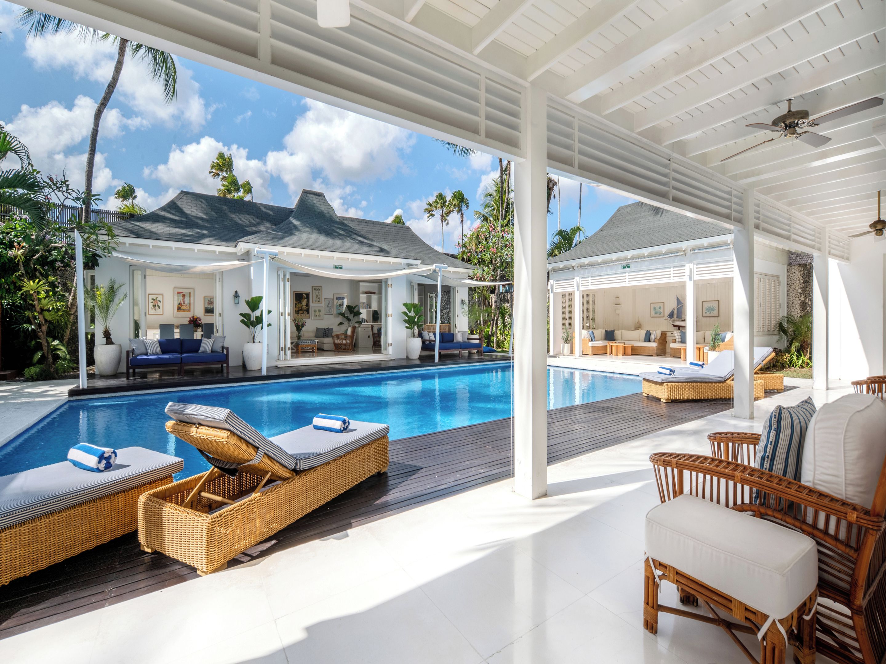 A poolside area with wicker lounge chairs, a covered seating area, and a view of a house with a balcony.