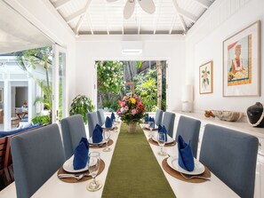 Un comedor con una larga mesa dispuesta para una comida, rodeada de sillas, y vistas a zonas verdes al exterior.