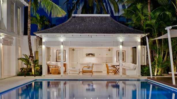 Un espace aménagé au bord de la piscine, comprenant un coin salon couvert, une table à manger et un coin cuisine.