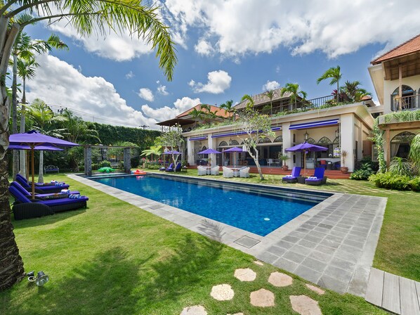 A swimming pool with lounge chairs and umbrellas, surrounded by a well-maintained lawn and tropical plants. - Sayang d’Amour (Seminyak)