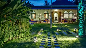 A tropical resort with a thatched-roof veranda, outdoor seating, and a well-lit garden with stepping stones. - Sayang d’Amour (Seminyak)