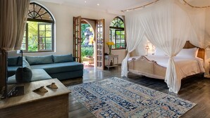 A bedroom with a canopy bed, a sofa, a small table, and a large window with curtains. - Sayang d’Amour (Seminyak)