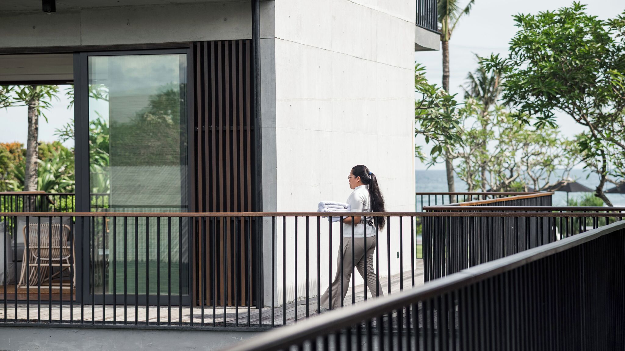 Een modern gebouw met grote ramen, een balkon met een metalen hekwerk en uitzicht op groen en een waterpartij.