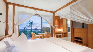 A bedroom with a large bed, a desk, a chair, and a TV. There is a balcony with a view of palm trees and the ocean. - Arnalaya Beach House (Canggu)
