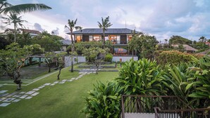 A modern house with a well-maintained garden, featuring a lawn, pathways, and various plants. - Arnalaya Beach House (Canggu)