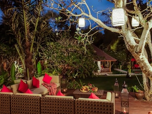 Relax in a serene outdoor lounge surrounded by lush greenery and a starry night sky.
