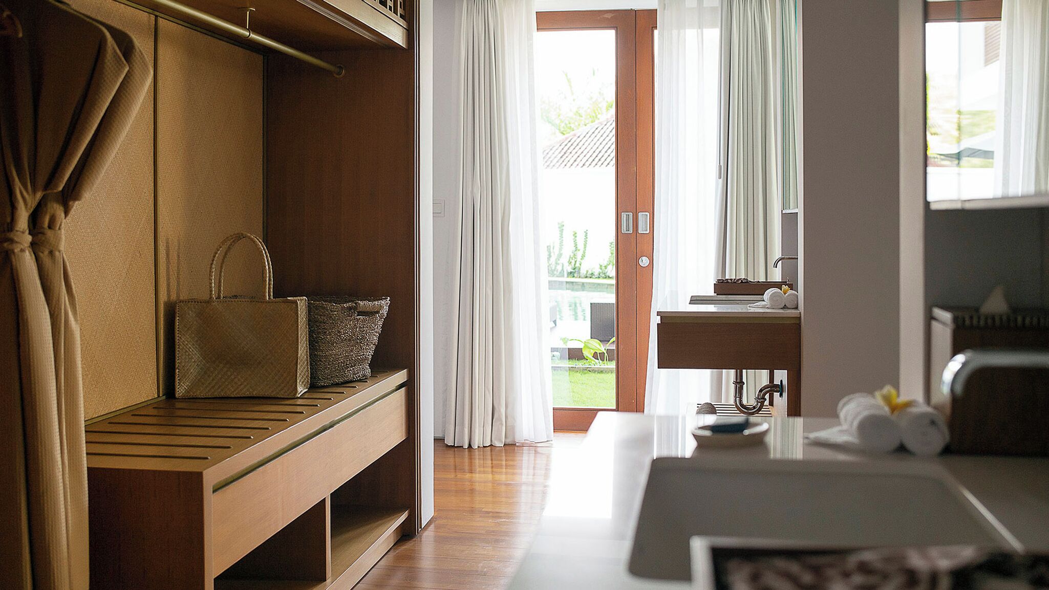 A modern hotel room with a wooden bench, a small table, a sink, and a view of the outdoors.