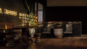A dimly lit room with a wooden table, two chairs, and a large vase with a plant. - Villa Indrani (Canggu)