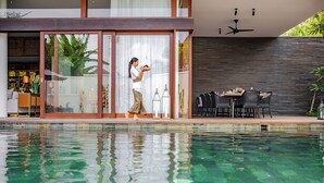 A modern house with a pool, a dining area with chairs and a table, and a person standing by the pool. - Villa Indrani (Canggu)