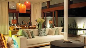 A modern living room with a white sofa, a round coffee table, and a dining area with a wooden table and chairs. - Villa Indrani (Canggu)