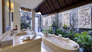 A bathroom with a freestanding bathtub, a large mirror, and stone wall decorations. - Villa Kakatua (Canggu)