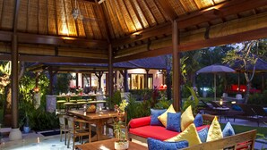 A covered outdoor seating area with a wooden table, chairs, and a sofa with patterned cushions. - Villa Kakatua (Canggu)