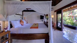 A four-poster canopy bed with a wooden frame and white bedding, a ceiling fan, and a view of the outdoor garden. - Villa Kakatua (Canggu)