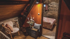 A cozy attic bedroom with a wooden sloped ceiling, a single bed with floral bedding, a wicker chair, and a small table with a vase of flowers. - Charming Riverside Cottage with Fishing & Wifi, Near Historic Sites (Rouez)