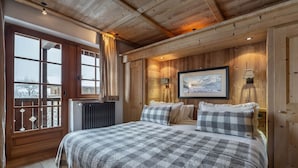 A cozy bedroom with a large bed, wooden walls, a window with curtains, and a framed picture on the wall.
