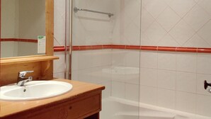 Un baño con tocador de madera, un lavabo blanco, cabina de ducha con mampara de vidrio y pared revestida de baldosas rojas.