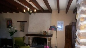 A cozy living room with a fireplace, a green armchair, a wooden coffee table, and a floor lamp. - Charming Farmhouse with Fireplace, Garden, and Modern Amenities in Joué-l'Abbé (Joué-l'Abbé)