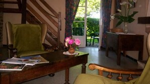 A cozy room with a wooden staircase, a green armchair, a wooden table with a vase of flowers, and a view through a door to an outdoor area with greenery. - Charming Farmhouse with Fireplace, Garden, and Modern Amenities in Joué-l'Abbé (Joué-l'Abbé)