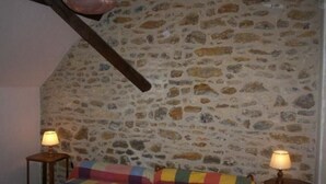 A bedroom with a stone wall, a colorful quilted bedspread, and two bedside lamps. - Charming Farmhouse with Fireplace, Garden, and Modern Amenities in Joué-l'Abbé (Joué-l'Abbé)