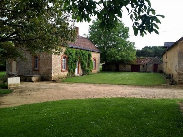 A stone building with a grassy courtyard, surrounded by trees and other structures.