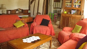 Een gezellige woonkamer met een houten plafond, een rode zithoek, een houten salontafel en een boekenkast.