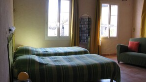 Een kamer met twee bedden, een groene bank, een klein tafeltje en een boekenkast.