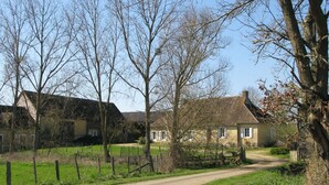 Een landweg die naar een huis met rieten dak en witte muren leidt.