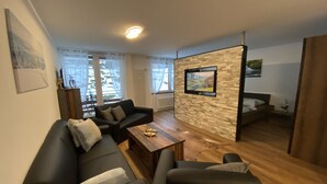 Ein modernes Wohnzimmer mit Sofa, Sesseln, Couchtisch und einem an einer Steinwand montierten Fernseher.
