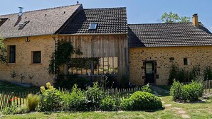 A rustic stone house with a tiled roof, a wooden porch, and a garden with a wooden fence. - Bucolic Country House near Le Mans (Louplande)