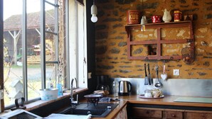 A kitchen with a large window, stone wall, wooden shelves, and various kitchen utensils. - Bucolic Country House near Le Mans (Louplande)