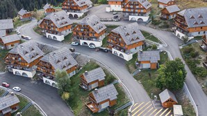 Un conjunto de edificios tipo chalet con varios pisos, conectados por caminos sinuosos, rodeado de colinas boscosas.