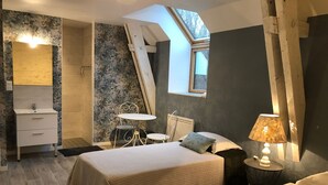 Et soveværelse med to senge, et ovenlys, et lille bord med en lampe og en stol.