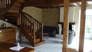 Eine Holztreppe führt zu einer Steinsäule, ein Holztisch mit einer Flasche und ein Sofa in einem Raum mit gefliestem Boden.