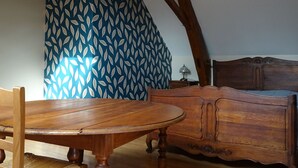 Ein Holztisch mit Stühlen, eine Holzkommode und ein gemustertes Vorhang in einem Raum mit geneigter Decke.