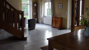 Ein geräumiges Zimmer mit einer Holztreppe, einem großen Fenster mit Vorhängen, einem Heizkörper und einem Holzkasten.