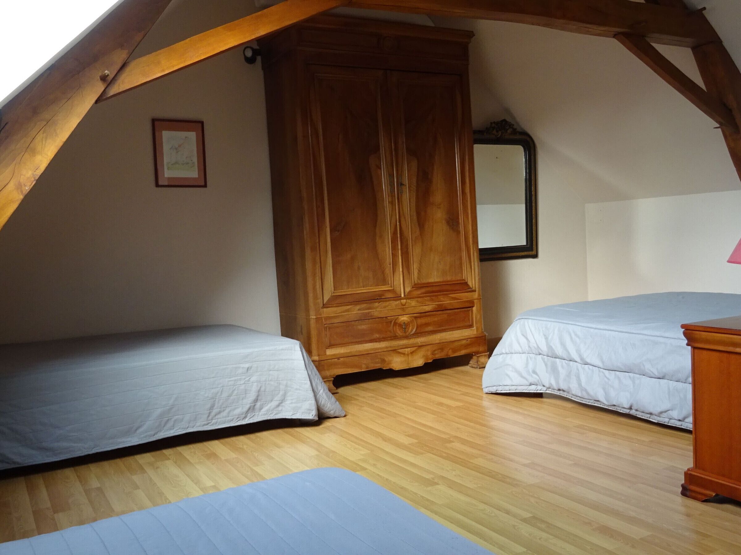 A bedroom with two single beds, wooden wardrobe, and a mirror on the wall.