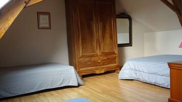 A bedroom with two single beds, wooden wardrobe, and a mirror on the wall.