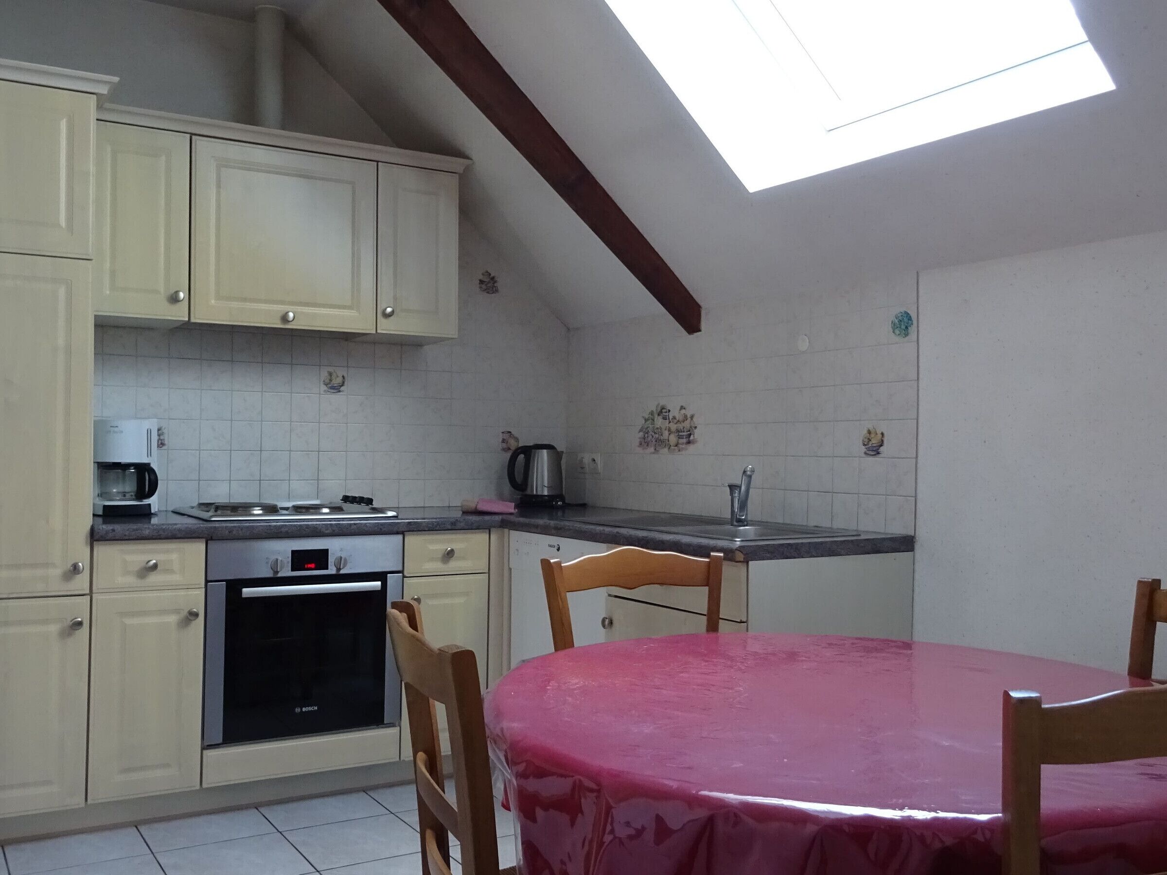 A kitchen with a dining table, cabinets, a Bosch oven, a coffee maker, and a skylight.