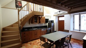 A kitchen with wooden cabinets, a dining table with chairs, a staircase, and a window with a view.