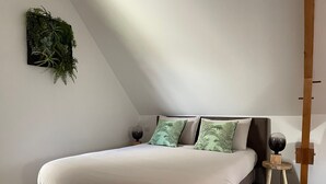 A modern bedroom with a bed, two pillows, a small stool, and a wall-mounted plant.